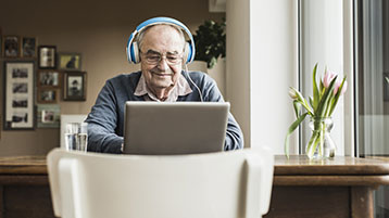 An older man, wearing headphones, using a computer